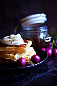 Australian Lilly-Pilly-Riberry jam on a black background, served with waffles and cream.