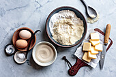 An assortment of baking ingredients, including eggs, flour, sugar, butter and vanilla pods, is arranged on a marble slab.