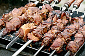 Saftig gegrillte Fleischspieße auf dem Grill. Marinierte Fleischstücke braten auf Metallspießen über heißen Kohlen. Traditionelle BBQ-Methode.