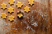 Star-shaped raw shortcrust pastry biscuits lie on a wooden cutting board, ready for baking. View from above.