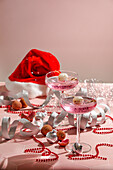 festlich gedeckter Neujahrstisch, zwei rosafarbene Cocktails garniert mit Litschi und Häppchen, rote Perlen, silberne Bänder, funkelnde Ornamente, für Weihnachtsfeiern
