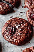 Close-up of freshly baked chocolate biscuits with a shiny chocolate centre and sprinkled sea salt, resting on parchment paper.