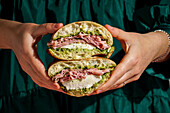 Delicious Italian mortadella sandwich with pesto and mozzarella basil pesto, crusty ciabatta bread, in your hands, in front of a deep green fabric background