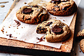 Close-up of freshly baked chocolate biscuits on parchment paper, with one biscuit partially bitten into and showing a sticky interior.