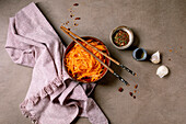 Korean and Asian cuisine dish: vegetable salad with marinated carrots and garlic. Served in a ceramic bowl with chopsticks. Spices in small bowls on the table with mocha mousse notes. Healthy food. Close-up