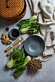 Bowl of soba noodles in a spicy broth with baby bok choy, surrounded by fresh mushrooms and ginger