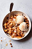 A bowl of apple crumble topped with two scoops of vanilla ice cream and some cinnamon.