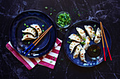 Steamed Japanese vegetable gyoza dumplings with soya, sesame oil and rice vinegar sauce on a black marble background.