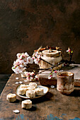 Traditional Asian tea ceremony with ceramic teapot, cherry blossom branches and Japanese sweet sesame cream sweets on a wooden table against a rustic brown background. Aesthetic Wabisabi style.