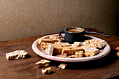 Traditional Spanish dessert, classic soft orange turron and crunchy almond turron, cut into pieces on a rustic clay plate. Espresso in a black cup, wooden table, copy room.