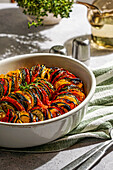 schön angerichtetes Ratatouille mit geschnittenen Zucchini, Auberginen, Tomaten und gelben Paprika, garniert mit frischen Kräutern. Warmes Sonnenlicht unterstreicht die gemütliche Atmosphäre