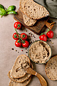 Homemade slices of sourdough bread with liver pâté, fresh cherry tomatoes on grapevines, basil leaves and spices on a wooden cutting board. Rustic breakfast ambience.