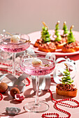 festlich gedeckter Neujahrstisch, zwei rosa Cocktails garniert mit Litschi und Häppchen, rote Perlen, silberne Bänder, funkelnde Ornamente, für Weihnachtsfeiern