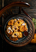 Pumpkin donuts, Spanish dessert, Bu?uelos de calabaza, la receta tradicional valenciana, placed on a wooden chair. The dark background, autumnal theme, large pumpkin under chair