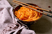 Korean and Asian cuisine dish: vegetable salad with marinated carrots and garlic. Served in a ceramic bowl with chopsticks. Spices in small bowls on the table with mocha mousse notes. Healthy food. Close-up