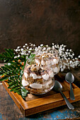 Classic Italian tiramisu, layered with cocoa powder and almonds in two glasses. Served on a tray with spoons on an old wooden table. Decorated with white baby's breath flowers and green leaves.