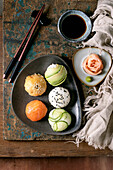 Temari sushi. Trendy sushi balls with salmon, avocado, cucumber and Japanese omelette on a brown ceramic plate. Soya sauce, pickled ginger, chopsticks, linen napkin on a rustic wooden base. View from above.