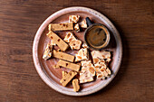 Traditional Spanish dessert, classic soft orange turron and crunchy almond turron, cut into pieces on a rustic clay plate. Espresso in a black cup, wooden table, copy room.