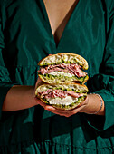 Delicious Italian mortadella sandwich with pesto and mozzarella basil pesto, crusty ciabatta bread, in your hands, in front of a deep green fabric background