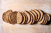 Freshly baked, artisan sourdough bread, sliced into portions on a wooden background. The crispy, rustic loaf with an airy texture shows the natural fermentation pattern.