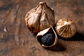 Whole black fermented garlic and peeled garlic clove on a dark wooden table. Healthy nutrition, spicy cooking ingredients, Asian cuisine
