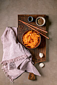 Korean and Asian cuisine dish: vegetable salad with marinated carrots and garlic. Served in a ceramic bowl with chopsticks. Spices in small bowls on the table with mocha mousse notes. Healthy food. Close-up