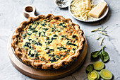A delicious spinach quiche with a golden crust, served on a wooden board with fresh spinach and sliced leek.
