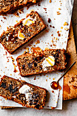Slices of banana bread, topped with butter and honey on parchment paper.