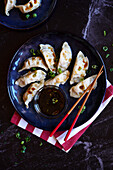 Steamed Japanese vegetable gyoza dumplings with soya, sesame oil and rice vinegar sauce on a black marble background.