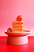 Stack of pink vanilla cake slices with strawberries. Pop art food colour blocking aesthetic.