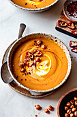 A bowl of creamy carrot soup, garnished with red pepper strips, crispy chickpeas and a cream swirl, served on a rustic plate.