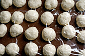 Mit Frischhaltefolie abgedeckte rohe Teigkugeln auf einer braunen Fläche. Gärender Brotteig, vorbereitet zum Backen von frischem Gebäck.