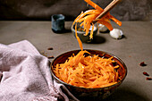 Korean and Asian cuisine. A man's hand uses chopsticks to pick up vegetable salad with marinated carrots and garlic from a ceramic bowl. Spices in small bowls on a table with mocha mousse tones. Healthy food