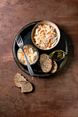Traditional starter Sauerkraut with carrots in a bowl and glass. Sea salt, olive oil, sliced rye bread and fork nearby. Healthy food, fermented products. Brown textured background, top view.