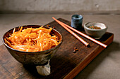 Korean and Asian cuisine dish: vegetable salad with marinated carrots and garlic. Served in a ceramic bowl with chopsticks. Spices in small bowls on the table with mocha mousse notes. Healthy food. Close-up