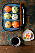 Temari Sushi. Trendy sushi balls with salmon, avocado, cucumber and Japanese omelette on a blue plate. Soya sauce, pickled ginger, chopsticks on a rustic wooden table.