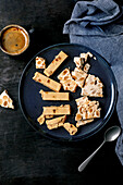 Traditional Spanish dessert classic: soft orange turron and crunchy almond turron, cut into pieces on a blue ceramic plate. Linen napkin, espresso coffee in black cup, black wooden background, top view.