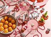 Festlicher Neujahrstisch, zwei rosafarbene Cocktails, garniert mit Litschi und Vorspeisen, rote Perlen, silberne Bänder, funkelnde Ornamente, für Weihnachtsfeiern