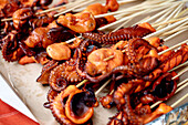 Close-up of grilled baby octopus on wooden skewers. Grilled seafood with pieces of charred octopus, showing off the texture of the tentacles. Street food of the Mediterranean cuisine.