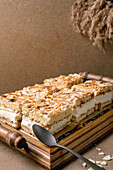 Homemade Norwegian sweet cake Verdens Beste Kake with pudding, meringue and almonds, cut into squares, served on a wooden tray. Beige-coloured table, close-up.