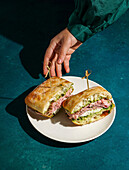 Delicious Italian mortadella sandwich with pesto and mozzarella basil pesto, crusty ciabatta bread, in your hands, in front of a deep green fabric background