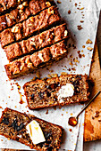 Sliced banana bread, topped with walnuts and served with butter and syrup on parchment paper.