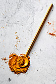Ein goldener Löffel, gefüllt mit gemahlener Kurkuma, liegt auf einer hellgrauen Marmorfläche.