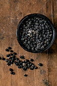 Black salted fermented Campota pepper in a black ceramic bowl on a dark wooden table. Healthy food, spicy cooking ingredients, Asian cuisine. View from above