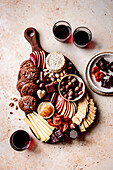 Ein elegantes Charcuterie-Brett mit verschiedenen Käsesorten, Keksen, Früchten, Nüssen und Pralinen, begleitet von einem Glas Rotwein.