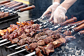 A chef grills juicy meat skewers on a charcoal grill. A person wearing gloves turns the skewers. Smoke comes from pieces of grilled beef on wooden skewers.