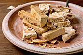 Traditional Spanish dessert, classic soft orange turron and crunchy almond turron, cut into pieces on a rustic clay plate. Espresso in a black cup, wooden table, copy room.