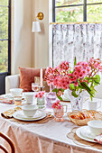 Gedeckter Frühstückstisch mit gestreifter Tischdecke und rosa Eukalyptusblüten