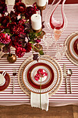 Festlich gedeckter Tisch mit roten Blumen, gemustertem Geschirr und gestreifter Tischdecke