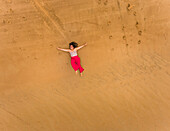 Aerial view of a happy woman lying on the beach of Cajueiro, Brazil.